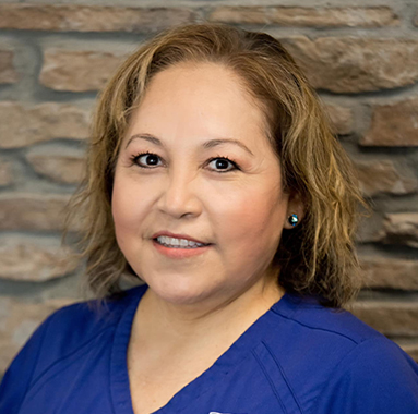 Professional headshot of woman in blue scrubs against brick wall backdrop for dental practice.