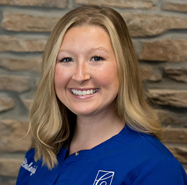 Smiling female dental professional in blue scrubs against brick background at Cronin Dentistry.