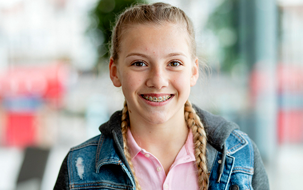 Smiling young girl wearing denim jacket and pink shirt in bright, modern dental office setting.