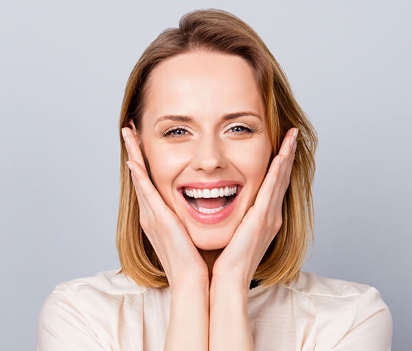 Smiling woman touching her face against neutral background, showcasing dental health and happiness.