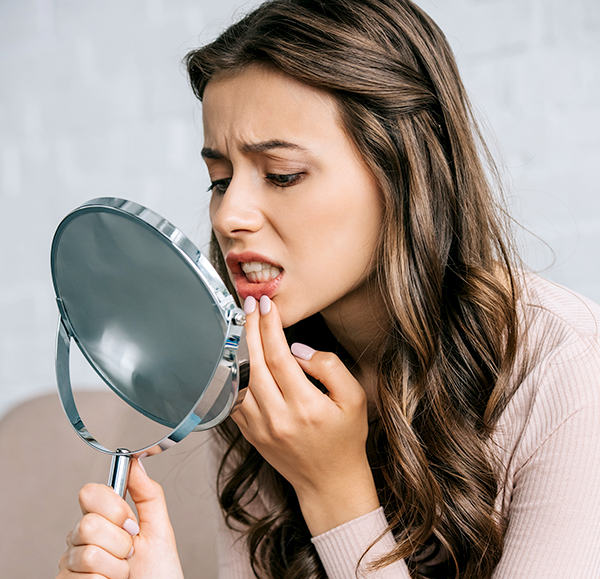 Woman examining her teeth in mirror, touching lip with finger in dental care setting.
