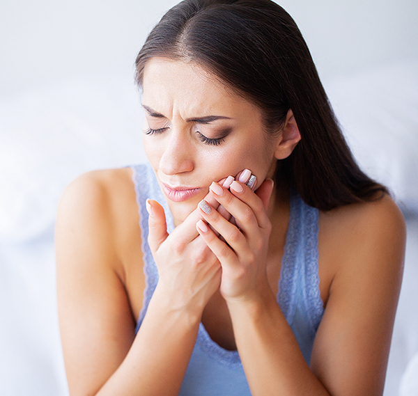 Woman holding cheek in pain, appearing to have tooth or jaw discomfort indoors.