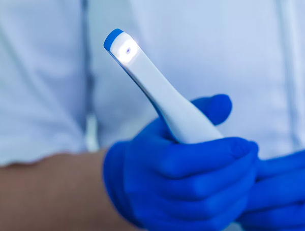 Dental professional in blue gloves holding intraoral camera for oral examination.