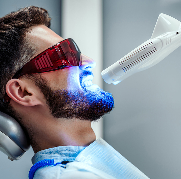 Man receiving dental treatment with blue LED light in modern dental office setting.