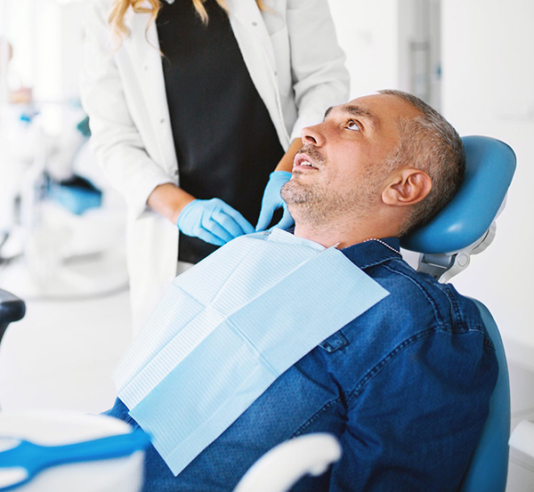 Male patient reclined in dental chair wearing bib during examination with dentist.