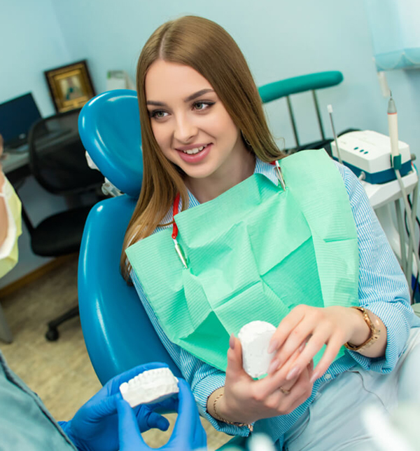 Young woman in green bib smiling in dental chair holding dental model