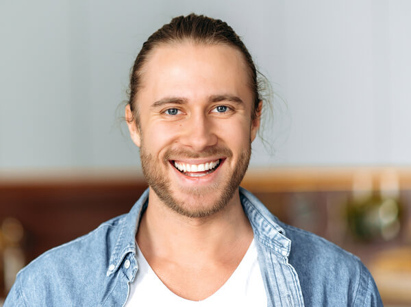 Male dental professional smiling at camera in modern dental office setting wearing blue shirt.