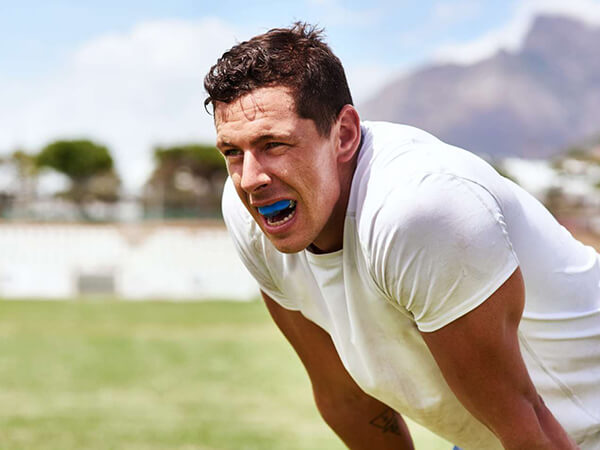 Man in white shirt smiling outdoors on grass field during sunny day.