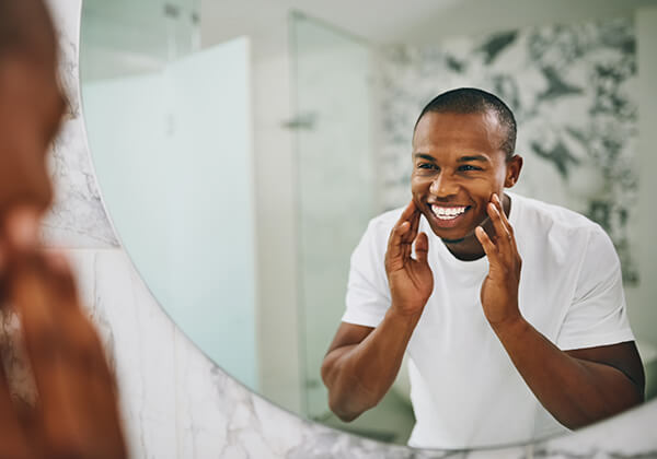 Man applying skincare product to face in bathroom mirror at home.