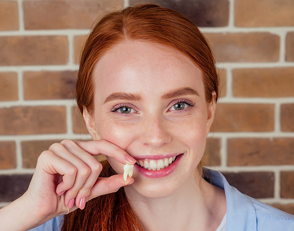 Young woman with red hair smiling brightly against brick wall background, pointing to teeth.
