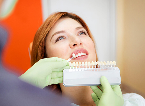 Dental professional holding tooth shade guide against patient's teeth during color matching consultation.