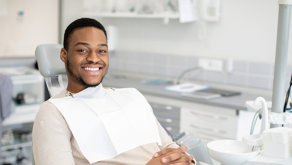 Smiling male patient holding dental bib in modern dental office treatment room.