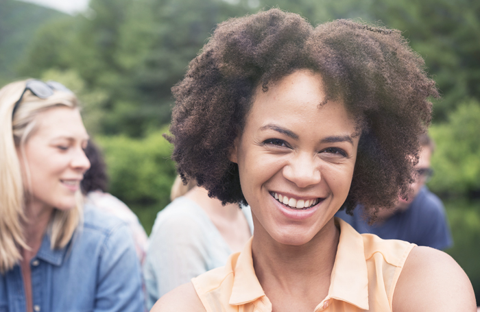 Smiling woman with curly hair outdoors with friends in natural setting, dental wellness theme.