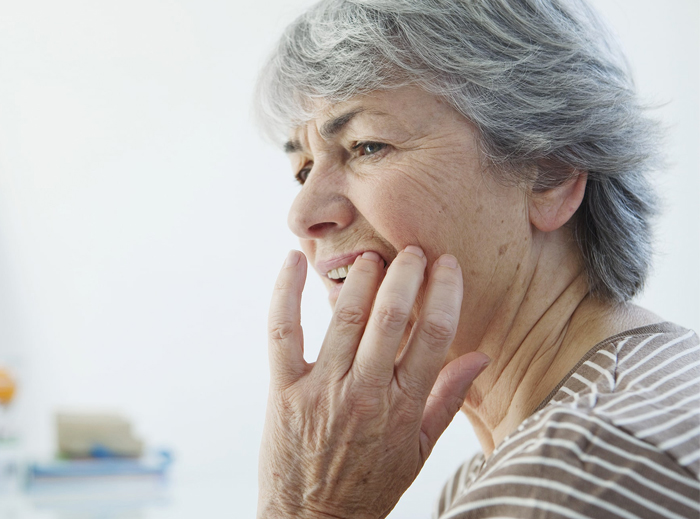 Older woman with gray hair touching her cheek in discomfort, suggesting dental pain or concern.