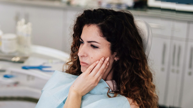 Woman with hand to cheek experiencing tooth pain in dental office setting.