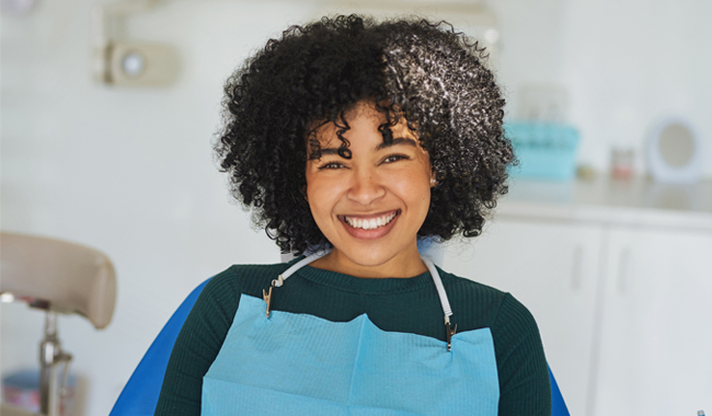 Smiling dental professional wearing blue apron in modern dental office setting.