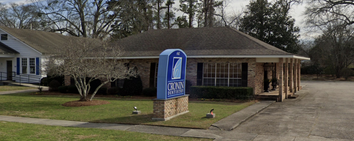 Cronin Dentistry exterior entrance with blue door sign, brick building, and landscaped front yard.