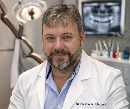 Dr. Steven A. Chimenti in dental office with X-ray images and equipment visible behind him.